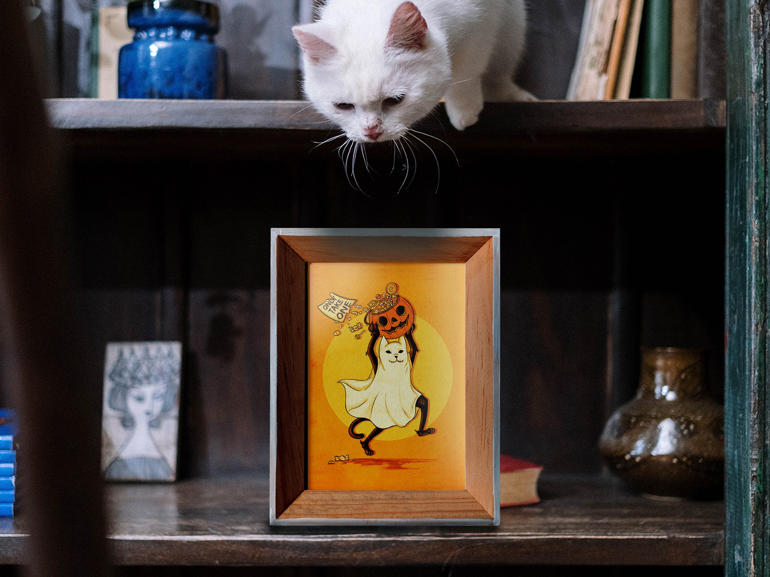 Halloween cat art poster in frame depicting black ghost cat stealing pumpkin with candy with an  "Only take one" sign in front of an orange wall surrounded by different pumpkins and jack o lanterns