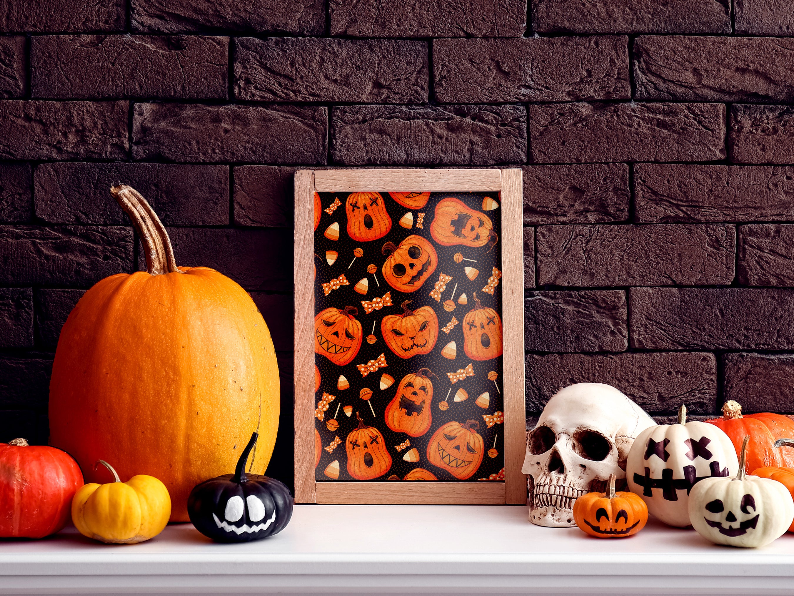 halloween pumpkin pattern art print within elegant black frame in front of black wall sitting ontop of brown counter surrounded by halloween decor such as candles, papers, potted plant, and a black skull