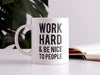 white work hard and be nice to people mug  on white desk next to book in front of house plant