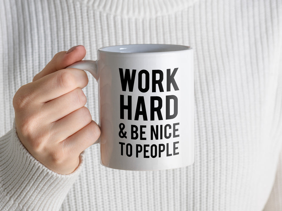 person in white sweater holding a white work hard and be nice to people mug