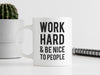 white work hard and be nice to people mug on white desk next to notebook and potted cacti in front of white background