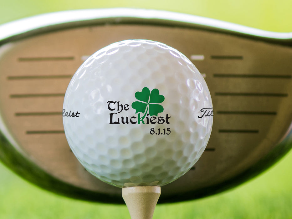 single white titleist golf ball with custom The Luckiest Design on beige tee in front of golf club with grass background