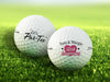 two white titleist golf balls with custom party and anniversary designs ontop of golf course grass background