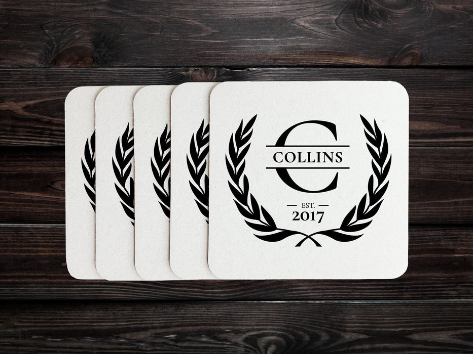 A stack of coasters are spread out on a dark wooden table. Coasters say Collins Est. 2017 with laurel design.