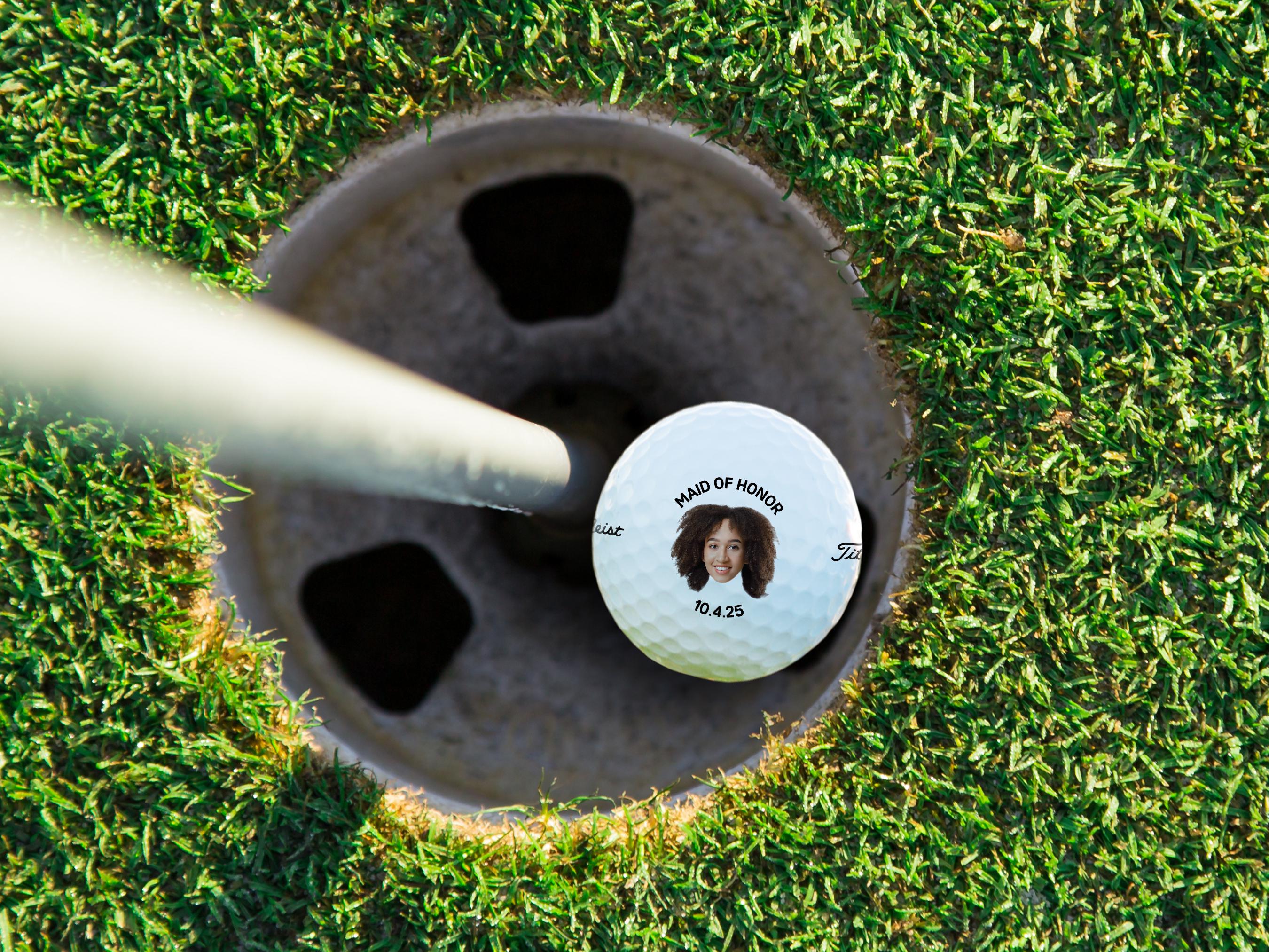 A golf ball with a picture of a smiling woman on it, placed on a grassy surface.