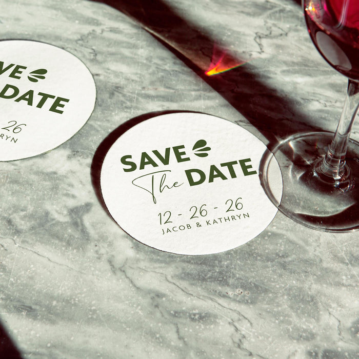 Personalized Save the Date coaster displayed beside a wine glass. Modern wedding favor customized with names and wedding date.