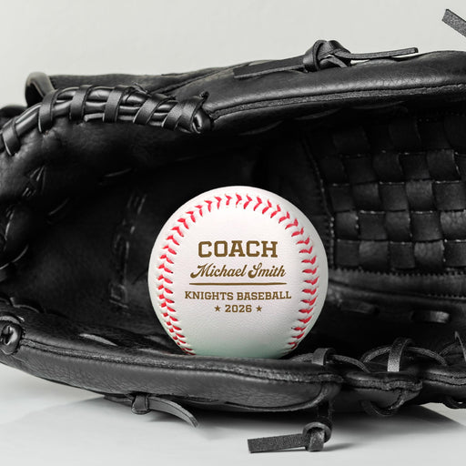A black baseball glove with a personalized baseball resting on top of it. The baseball design features Coach Michael Smith Knights Baseball 2026