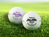 Two personalized golf balls with You're Tee-riffic Mom designs printed on them, placed on a grassy field.