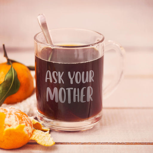 Clear glass mug filled with dark tea featuring the engraved phrase “Ask Your Mother” in bold frosted lettering. A warm lifestyle image with soft citrus accents creating a cozy everyday feel.