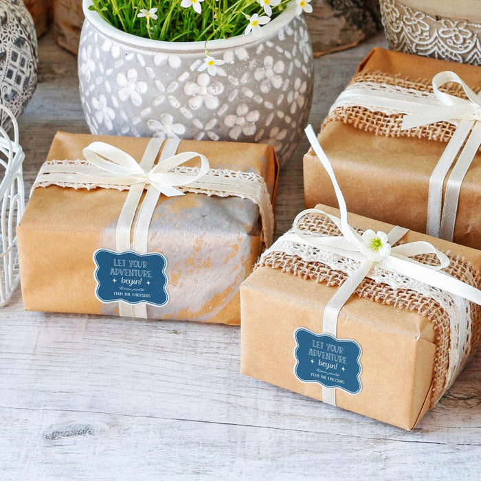 Small wrapped gift boxes decorated with personalized “Let Your Adventure Begin” wedding gift tags in white glitter. Elegant packaging inspiration for wedding favors and bridal shower gifts.
