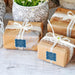 Small wrapped gift boxes decorated with personalized “Let Your Adventure Begin” wedding gift tags in white glitter. Elegant packaging inspiration for wedding favors and bridal shower gifts.