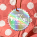 A rainbow hang gift tag with the text "Happy Holidays" UV printed on it, hanging from a string against a background of red and white polka dots.