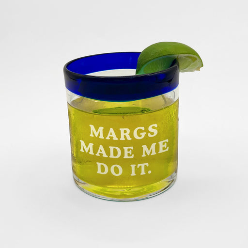 A glass filled with a margarita cocktail, with a lime wedge and a blue rim. The text on the glass reads "MARGS MADE ME DO IT."