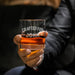Close-up lifestyle photo of a personalized whiskey glass held in hand, featuring the “Crafted For John” engraved design. The glass is filled with whiskey and ice, making it a perfect gift for whiskey lovers and home bar enthusiasts.