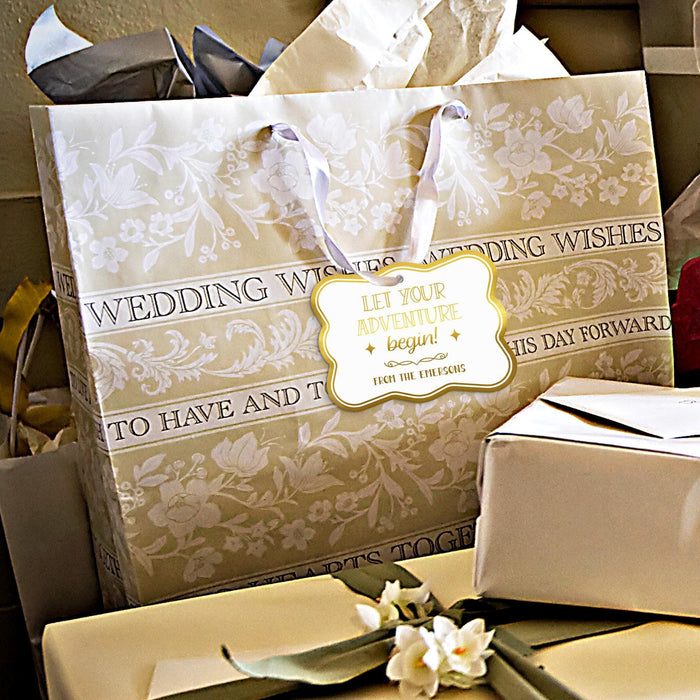 Gold foil “Let Your Adventure Begin” wedding gift tag attached to elegant wedding gift packaging. Styled with wrapped presents and neutral wedding décor for gifting inspiration.