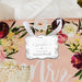 Floral wedding-themed flat lay featuring a personalized “Let Love Sparkle” wedding gift tag in metallic silver foil. Styled with soft flowers and romantic décor details.