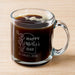 A glass mug filled with a dark liquid, likely coffee, with foam on top. The mug has an engraved message on it, which reads "Happy Mother's Day SCARLET, 2026".