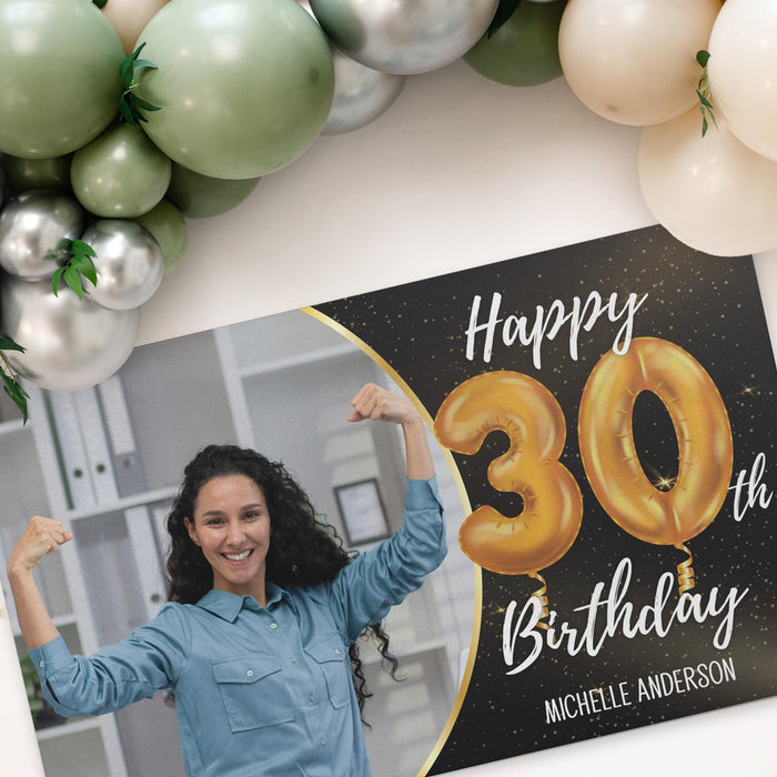 Black and gold birthday banner displayed beneath a balloon garland featuring a custom photo, age, and name.