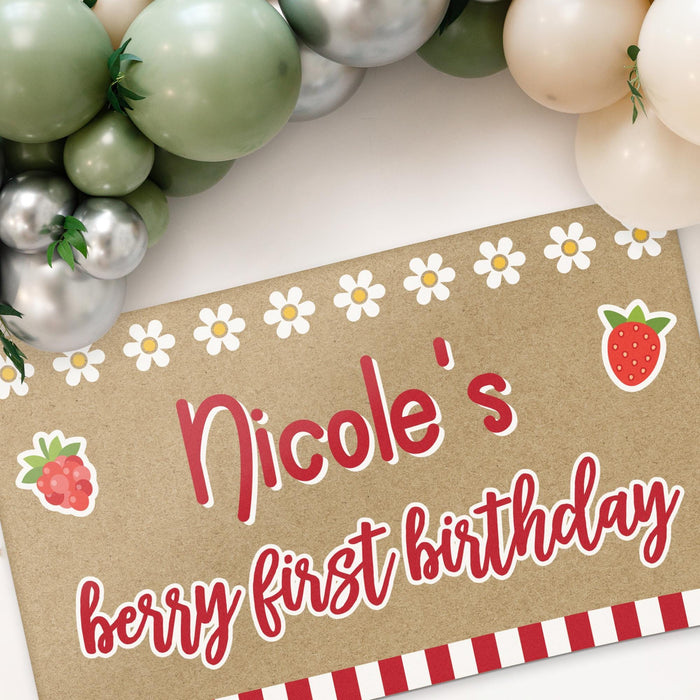 Large personalized first birthday banner hanging with party decorations featuring berry themed graphics and custom printed name.