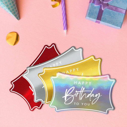 Four elegant script tags in metallic gold, metallic silver, metallic red, and metallic rainbow lying beside colorful gifts and party decorations.