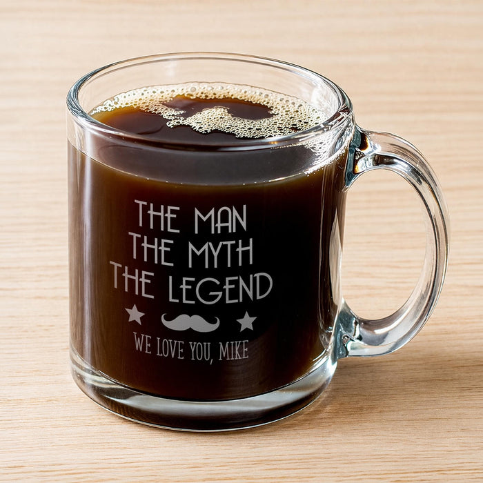 A glass mug filled with a dark liquid, likely coffee, with foam on top. The mug has a message engraved on it that reads "The man, the myth, the legend, we love you, Mike".