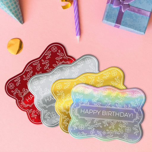 Four floral birthday gift tags in metallic gold, metallic silver, metallic red, and metallic rainbow lying beside colorful gifts and party decorations.