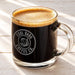 A glass mug filled with a dark, foamy beverage, likely coffee, with an engraving on the side that reads "Cool Dads Coffee Co.".
