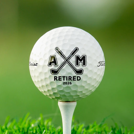 Personalized retirement golf ball featuring the Retired Monogram design with custom initials and retirement year. Displayed on a golf tee against a golf course background.