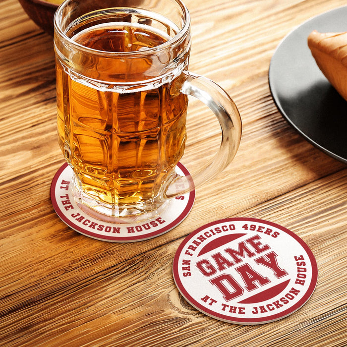 Red custom football coaster under a beer mug with another personalized Game Day coaster displayed beside it on a wooden table.