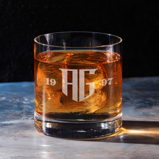 Clean hero-style image of the personalized whiskey glass on a marble surface, showcasing the “AG” monogram with split year design. The rich whiskey tones highlight the crisp engraved finish.