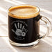 A glass mug filled with a dark liquid, likely coffee, with a foamy top. The mug has a handprint design and text that reads "Happy Mother's Day 2026 Love, Ella".