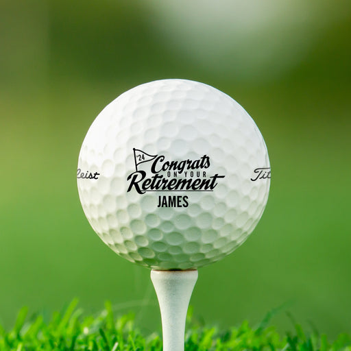 Single white Titleist golf ball with Congrats On Your Retirement design on white golf tee with golf course grass in the background