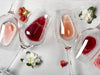 Four wine glasses lay on white wooden surface next to flowers. The glasses have Last Name and Established Date design engraved on it.