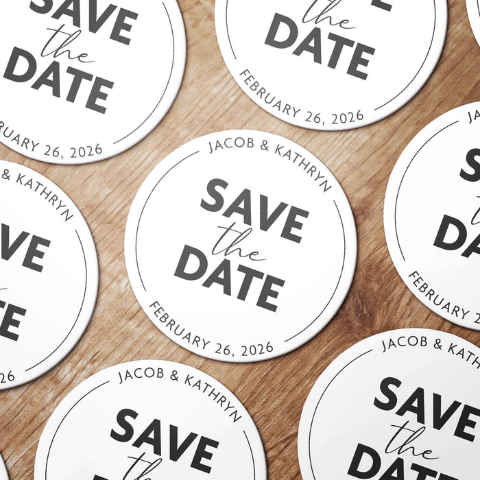 Personalized Save the Date coasters shown in a wedding favor arrangement. Features a modern typography design with custom names and date.