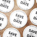 Personalized Save the Date coasters shown in a wedding favor arrangement. Features a modern typography design with custom names and date.