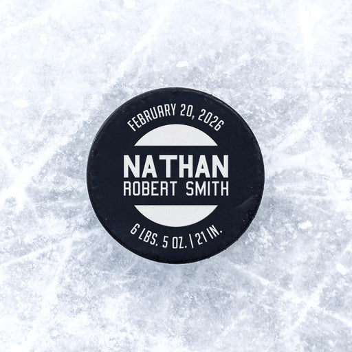Personalized hockey puck with a white UV printed birth announcement design displayed on an icy background.