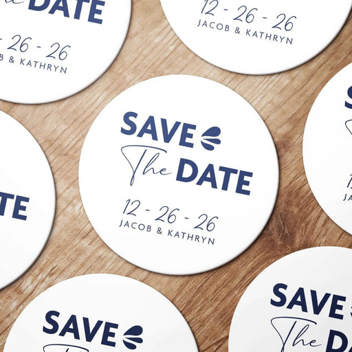 Personalized Save the Date coasters shown in a wedding favor arrangement. Features a modern typography design with custom names and wedding date.