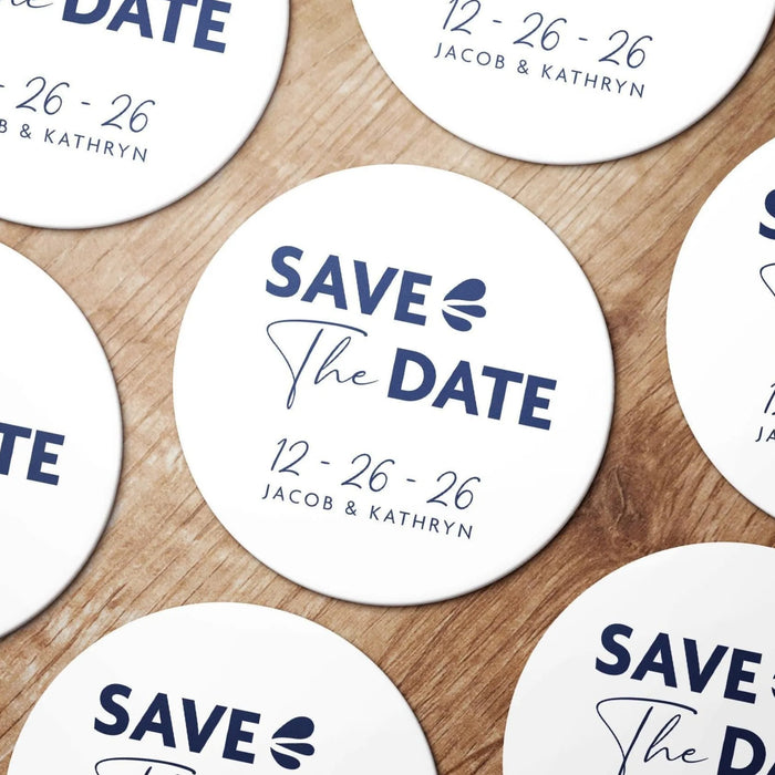 Personalized Save the Date coasters shown in a wedding favor arrangement. Features a modern typography design with custom names and wedding date.