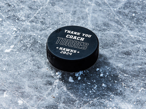 single hockey puck on blue ice rink with a white coach appreciation design that says Thank You Coach Torres, Giants, 2024