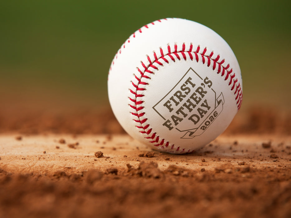 Baseball sits on field. Baseball has First Father's Day design engraved on it.