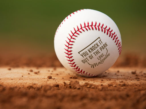 Baseball sits on field. Baseball has Knock It Out of the Park design engraved on it.