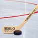 Personalized hockey stick displayed on an ice rink with baby name and birth details in a bold layout and puck icon, placed next to a real hockey puck.