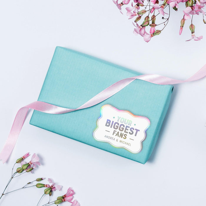 Pastel blue envelope styled with ribbon and a holographic rainbow “Your Biggest Fans” personalized wedding gift tag. A colorful presentation idea for wedding cards and small gifts.