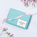 Pastel blue envelope styled with ribbon and a holographic rainbow “Your Biggest Fans” personalized wedding gift tag. A colorful presentation idea for wedding cards and small gifts.
