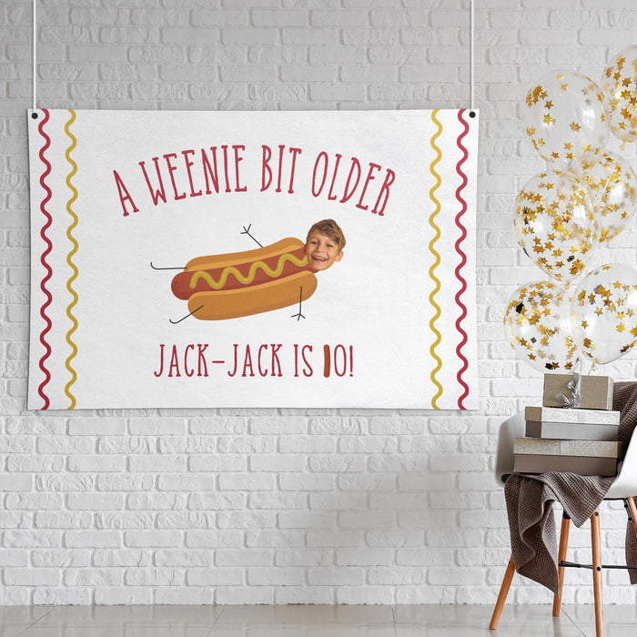 Personalized "A Weenie Bit Older" birthday banner displayed as wall décor on a white brick wall.