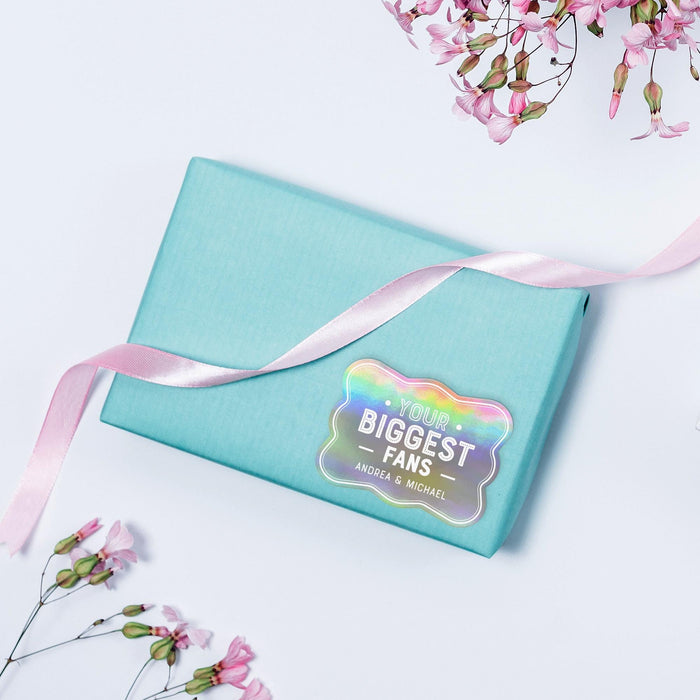 Small pastel gift box decorated with a rainbow foil “Your Biggest Fans” wedding gift tag tied with ribbon. A colorful and modern packaging idea for weddings and bridal showers.