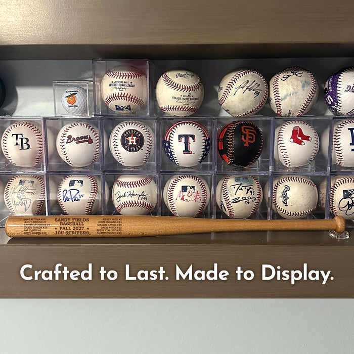 A collection of baseballs and a wooden mini baseball bat displayed on a shelf, with the caption "Crafted to Last. Made to Display."