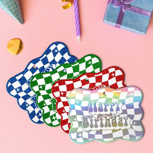 Four groovy checkered gift tags in metallic rainbow, glitter blue, glitter green, and glitter red lying beside colorful gifts and party decorations.