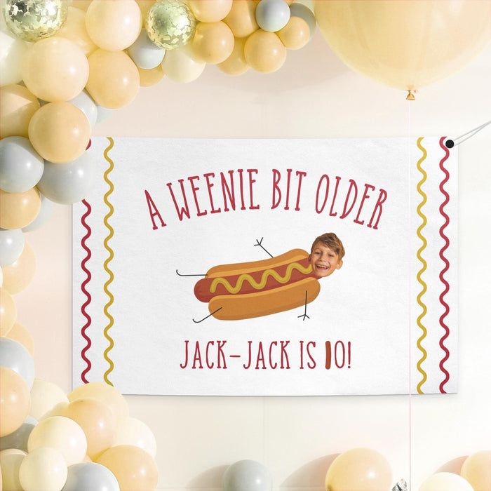 Hot dog birthday banner displayed as a party backdrop with gold and white balloon decorations.