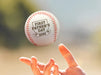 Person throws baseball into the air. Baseball has First Father's Day design engraved on it.